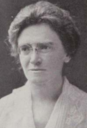 A middle-aged white woman, wearing pince-nez glasses and a white lace-collared blouse or dress